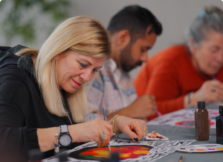 Woman focused on painting during an art activity with others nearby.