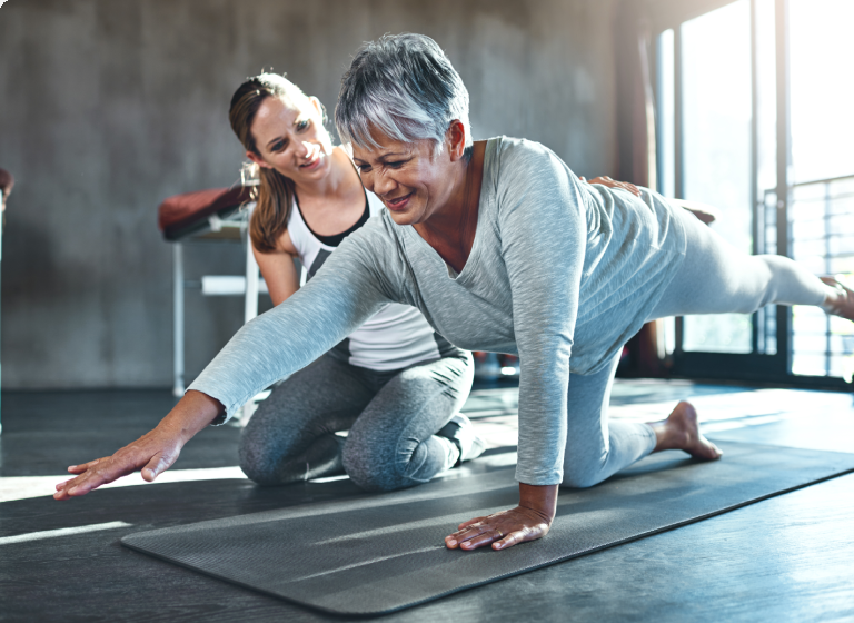 Senior woman doing yoga with a trainer's guidance.