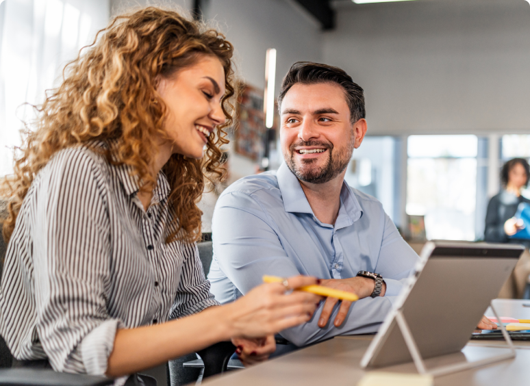 Two colleagues smiling while working together on a laptop.