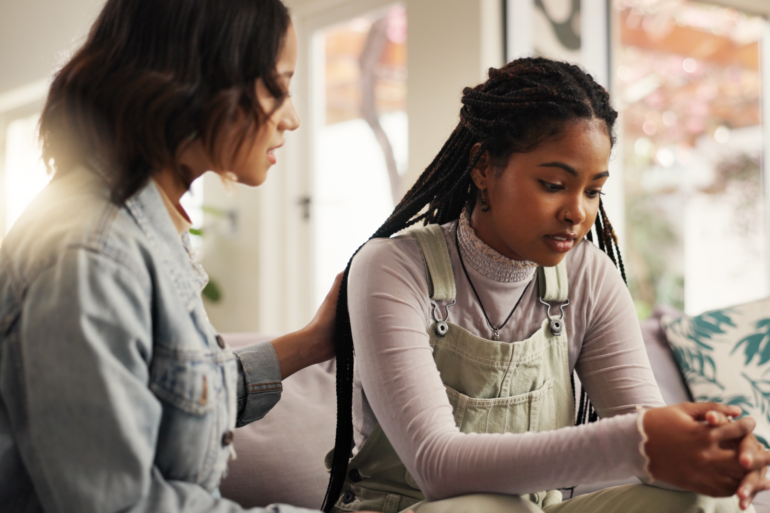 A comforting woman consoles a distressed young woman indoors.