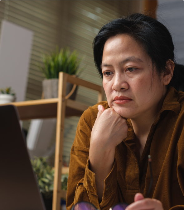 Woman thoughtfully looking at a laptop screen indoors.