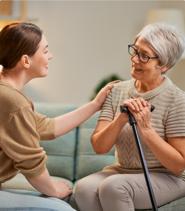 A young woman gently comforting an elderly woman with a cane.