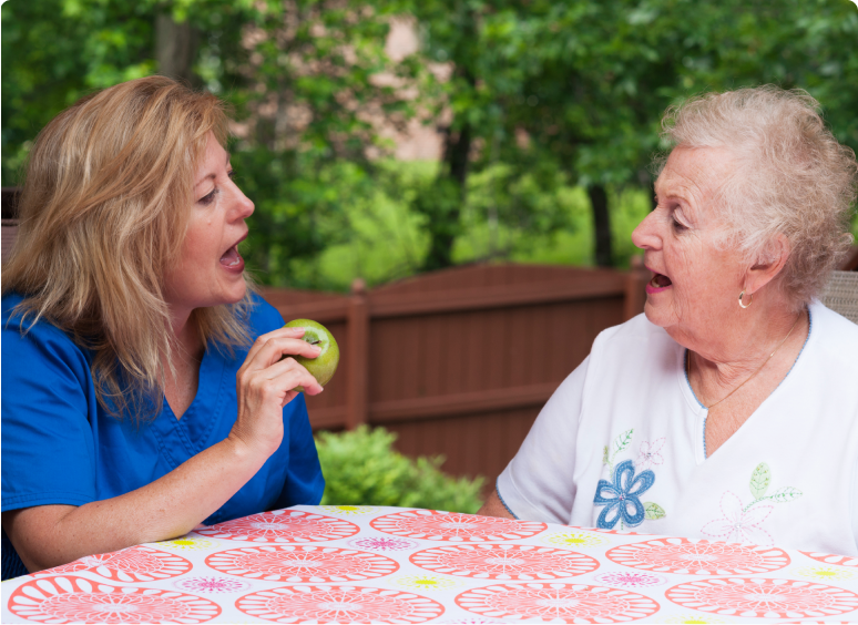 Two women sharing a joyful moment outdoors at a table.